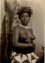 Studio portrait of a young Fijian woman with bare breasts, wearing a necklace of shell or bone and a headdress made of plants
