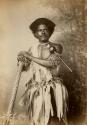 Studio portrait of a Fijian man wearing a decorated outfit and holding instruments