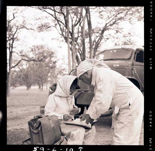 Lorna Marshall and Laurence Marshall wearing clothing and head coverings to protect against tsetse flies, and looking at Lorna's notebook