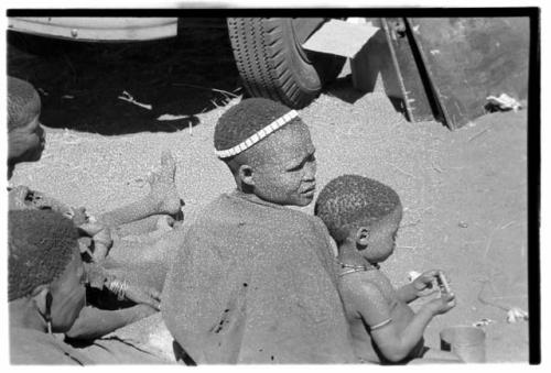 Di!ai ("/Qui Guide's" wife) sitting with her child, seen from behind, with two unidentified people sitting behind her