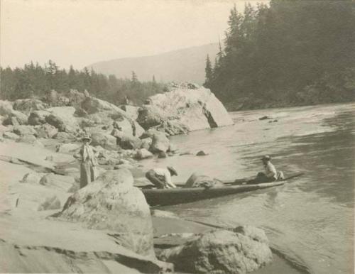 Two men loading a canoe while Miss Nicholson waits on shore on the Klamath River