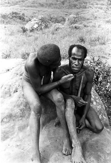 Shot of 2 men; one of them is cutting the other's beard with Robert Gardner's pen knife