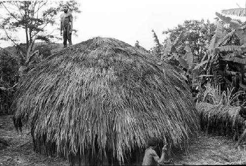 Man on the just thatched roof of a Honai at Abukulmo