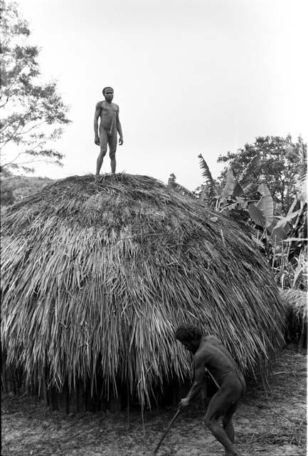 Man on the just thatched roof of a honai at Abukulmo