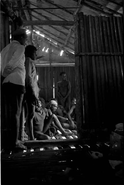 Men standng and seated in the government rest house in the village