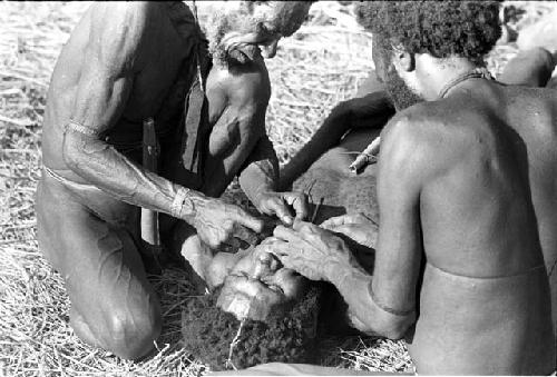 Yoli's beard being plucked by Tuessiké and one other man