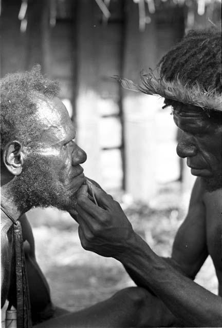 A man having his beard plucked by another man