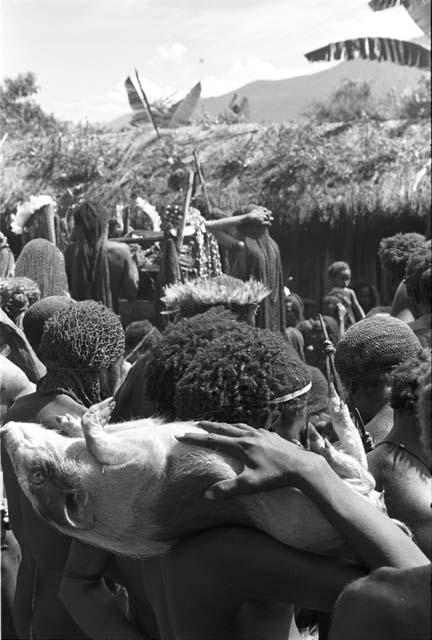 Over the heads of men as they mourn towards the pia; a man has a pig on his shoulder in the frgd