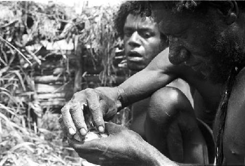 Woluklek watches as a man inspects a mouse in his hands