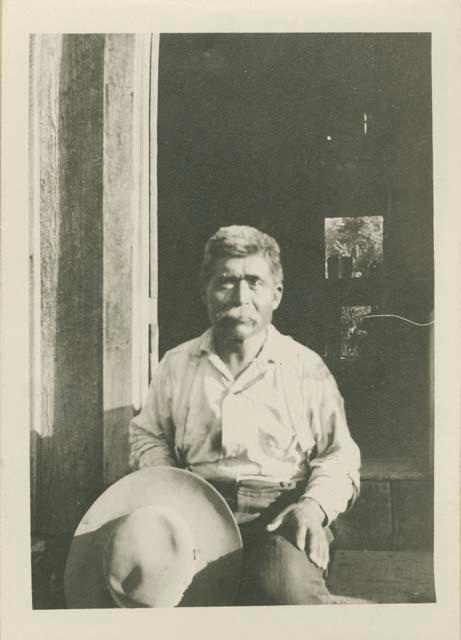 Billy Bennett, seated by a doorway holding his hat on his knee at Baird