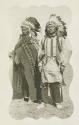 Two Jicarilla Apache men wearing large feather headdresses