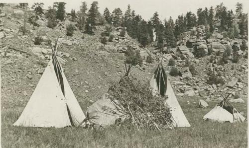 Four tepees with rocky, pine-covered hills in background