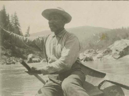 Yurok boatman rowing a canoe along shore