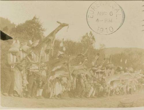 Yurok Indians in a line, each holding a deer skin up on a stick