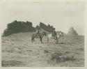 Two Navajo men on horses in front of wall