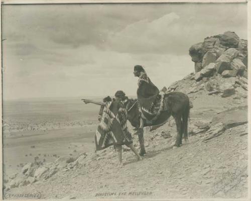 Navajo man points into the distance, with another man on a horse