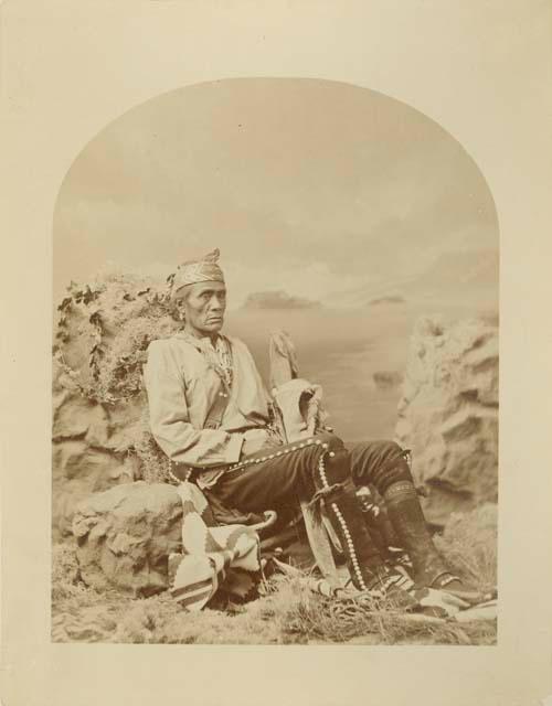 Studio-staged scene of a Narbona Primero (Navajo sub-chief) sitting against some rocks