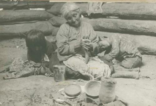 Navajo woman rolling clay, with two children sitting beside her