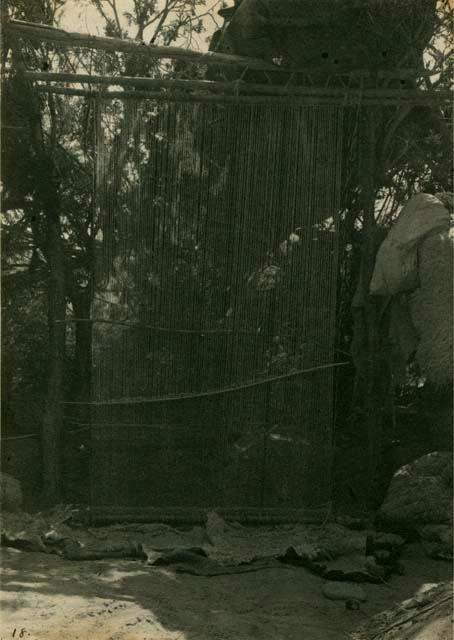 First step in blanket making; a loom stands upright with foundation of white wool stretched across it