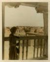 Tinted photograph of a woman in long striped skirt looking over balcony at pueblos