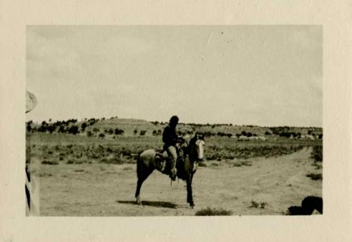 Man on horseback. Acoma Fire house in background