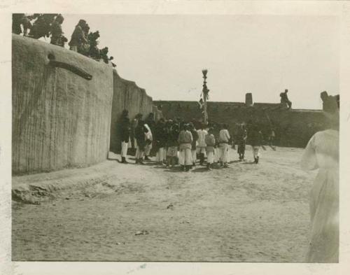 Singers and staff bearer outside kiva, Santo Domingo Pueblo. Dancers on roof