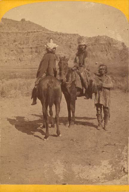 Two people on horseback, one standing alongside others. Kai-vav-its Tribe