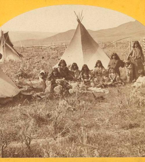 Group of people seated before tent.