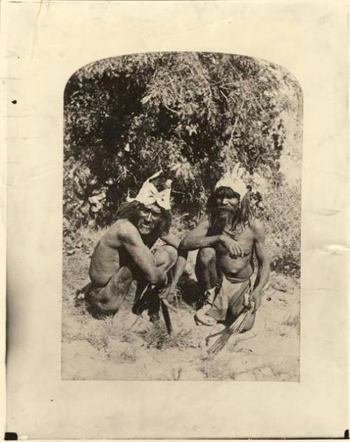 Two men crouched low to the ground, holding bow and arrows