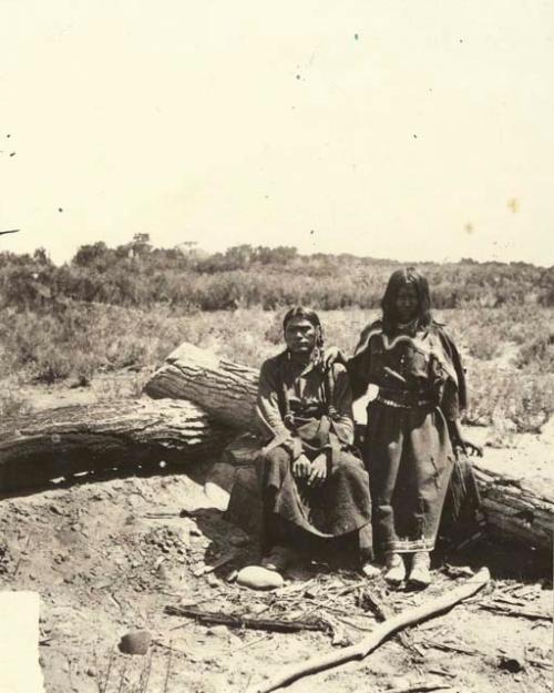 Two people seated on log.