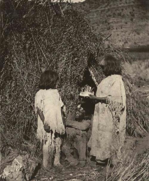 Woman placing headdress upon man, child at his other side