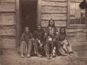 Portrait of 4 men, seated before door to a cabin