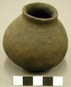 Ceramic miniature vessel, straight neck, rounded base, plain.