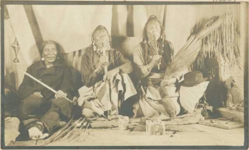 Three men seated inside tipi, Chief Greasy Forehead in center.
