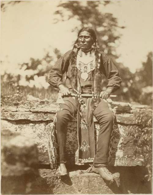 Man seated on rocks, wearing breast plate and holding axe in both hands