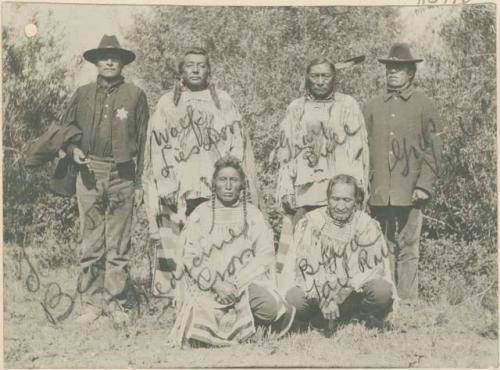 Four native American men and two men in Western dress posing for photograph; One wears a six pointed star