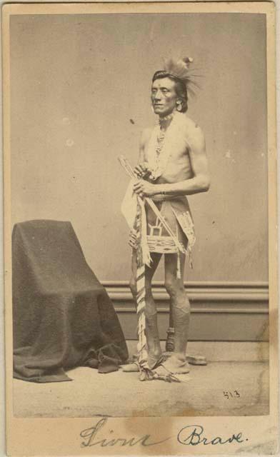 Studio portrait of man, full-length, standing next to covered chair