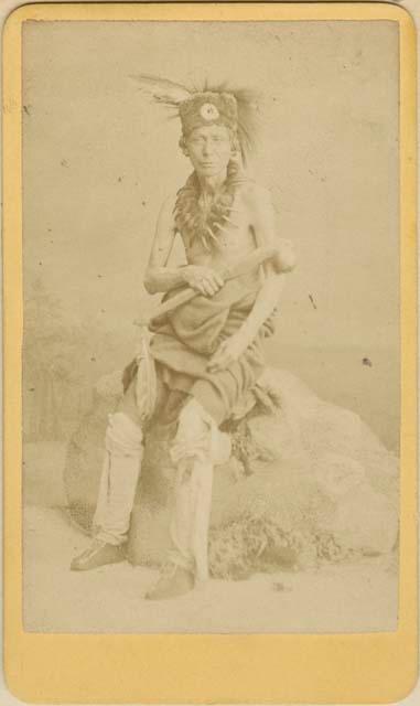 Full length studio portrait of man, seated on stone