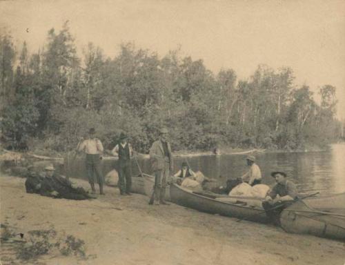 men on shore beside canoes