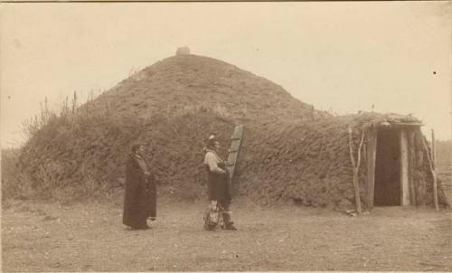 Woman and man walking alongside earth lodge