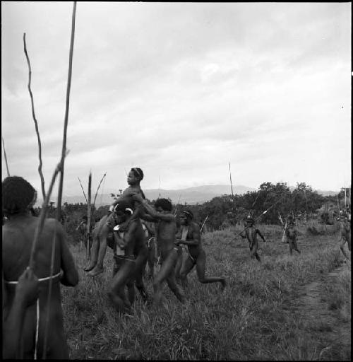 A group of men carrying a wounded young warrior to safety