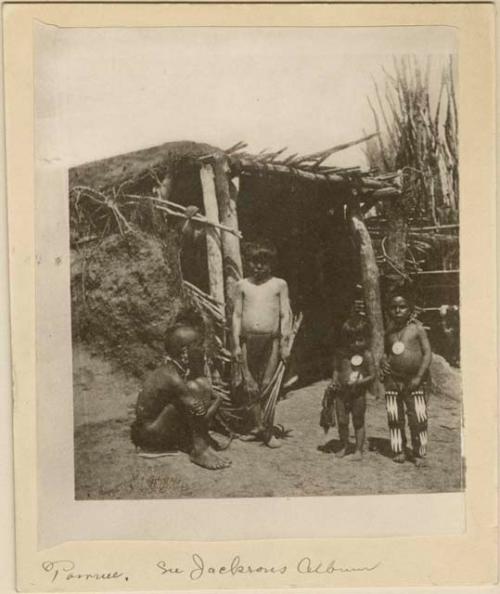 Four children before a dwelling, one boy is holding a bow and arrows