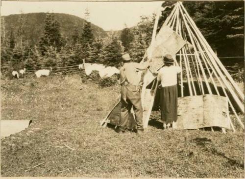 A man and woman laying bark strips on the frame of a Micmac wigwam