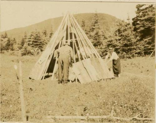 A man and woman laying on the bark strip covering of a Micmac wigwam