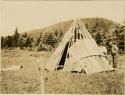 Man and woman laying on of bark strip covering over wigwam frame