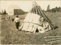 A man and woman laying on the bark strip covering over the frame of a wigwam