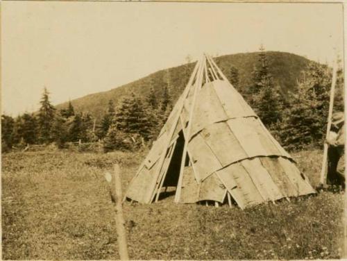 Man and woman putting poles on wigwam to hold down bark strips