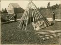 Boy watches as a man and woman lay bark covering over the frame of a wigwam