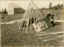 Boy watches as man and woman lay on bark strip covering of wigwam