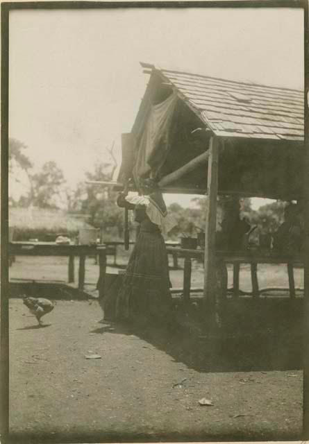 Woman grinding corn in mortar with pestle. Jack Tigertail's Camp